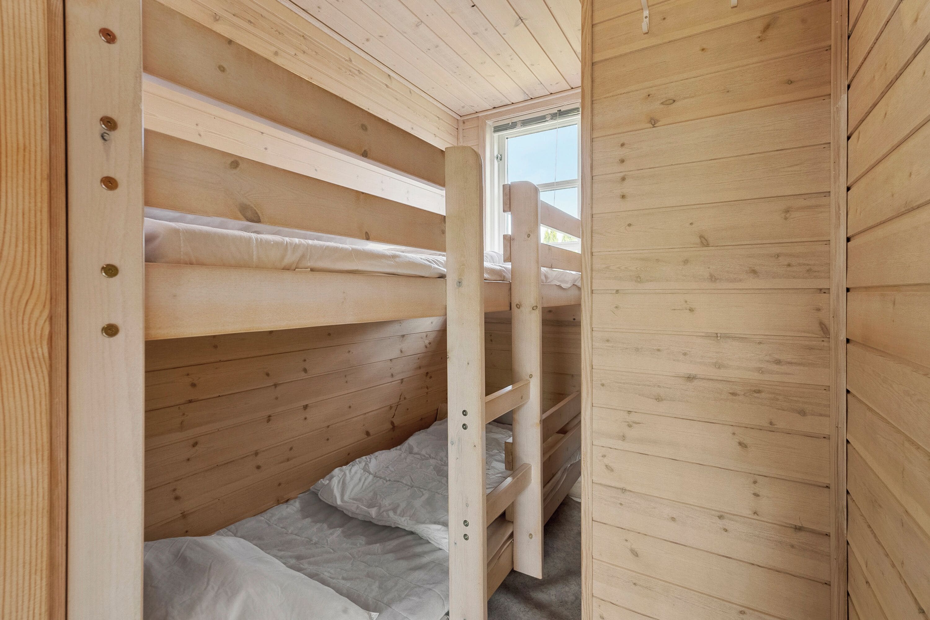 A wooden bunk bed room with a window, a door, and a ladder.