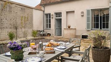 An outdoor dining area with a table set for breakfast, including bread, pastries, and a pitcher.