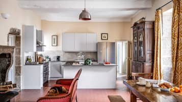 Una cocina con una isla central, un comedor con un banco, y un perro descansando en una silla.