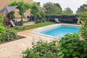 Ein rechteckiger Pool mit gefliestem Sonnendeck, umgeben von üppiger Bepflanzung und einer Steinmauer.