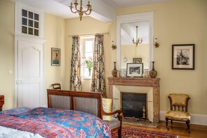 Ein Zimmer mit Bett, Kamin, Sessel und Spiegel.