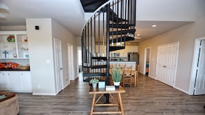 A spacious living area with a wooden floor, a black spiral staircase, and a dining area with wooden furniture.