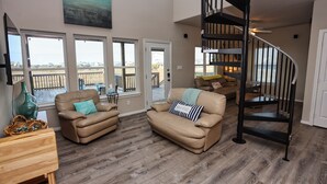 A spacious living room with a large window, a black spiral staircase, and a beige leather sofa.