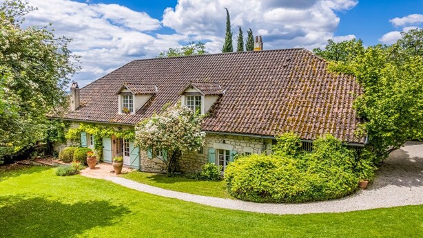A stone house with a tiled roof, surrounded by lush greenery and a well-maintained lawn.