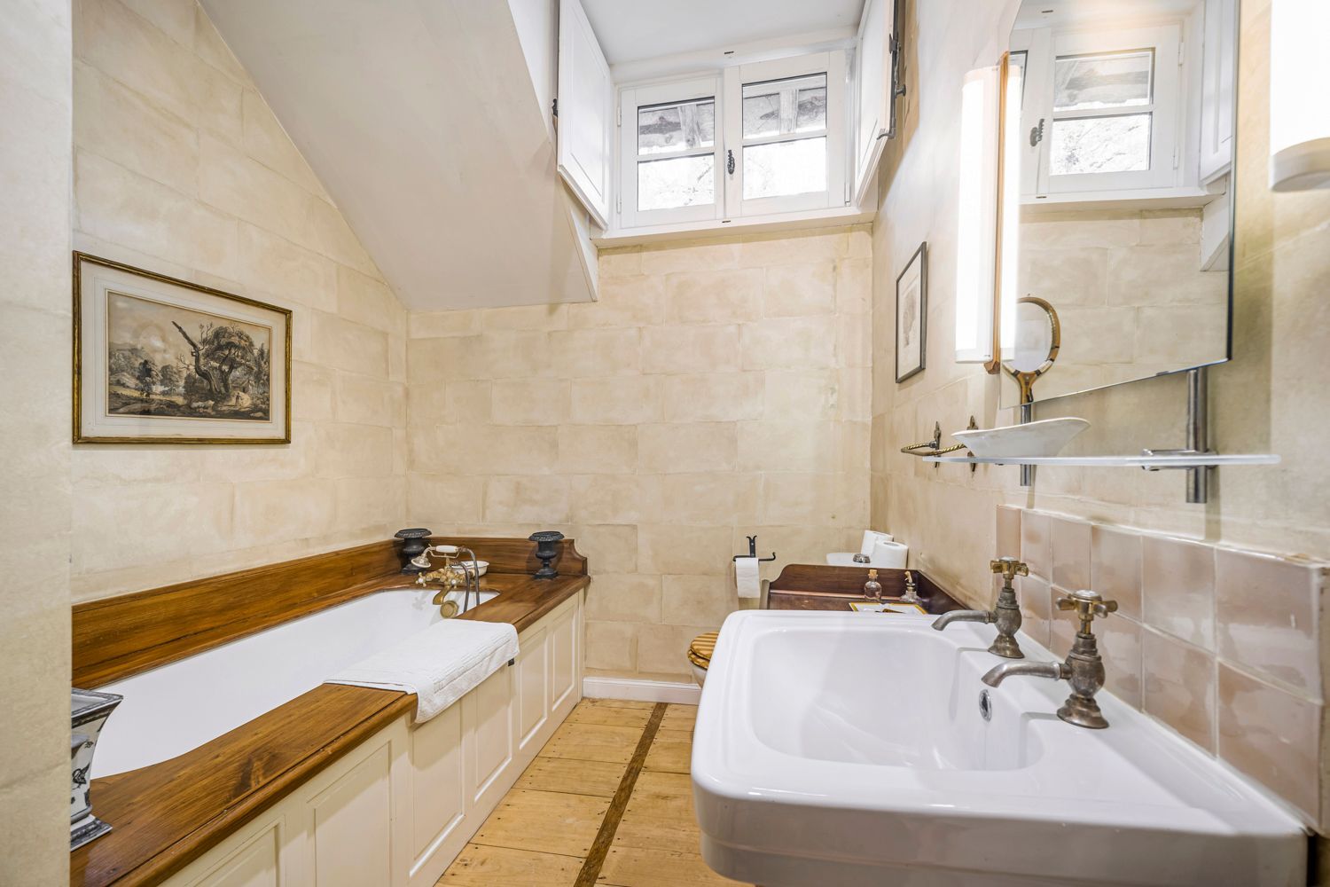A bathroom with a bathtub, a sink, and a shower area. There is a window above the shower, and a framed picture on the wall.
