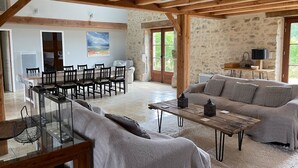 A spacious living area with a wooden ceiling, a stone wall, a dining area with a table and chairs, and a sofa with cushions.