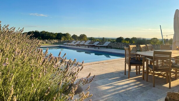 A pool area with lounge chairs and a table, surrounded by stone walls and vegetation.