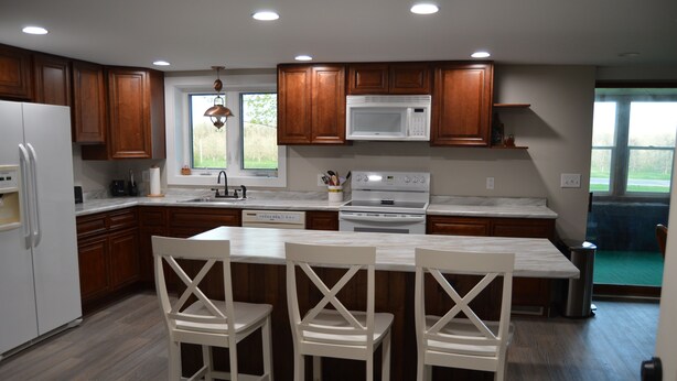 A modern kitchen with wooden cabinets, a white refrigerator, a built-in microwave, and a large island with bar stools.
