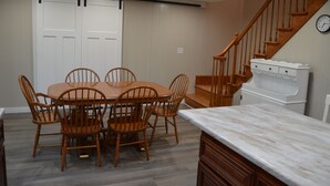 A dining area with a wooden table and chairs, a kitchen counter, and a staircase with a wooden railing.