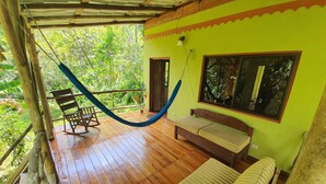 A wooden deck with a hammock, a bench, and a window overlooking greenery.