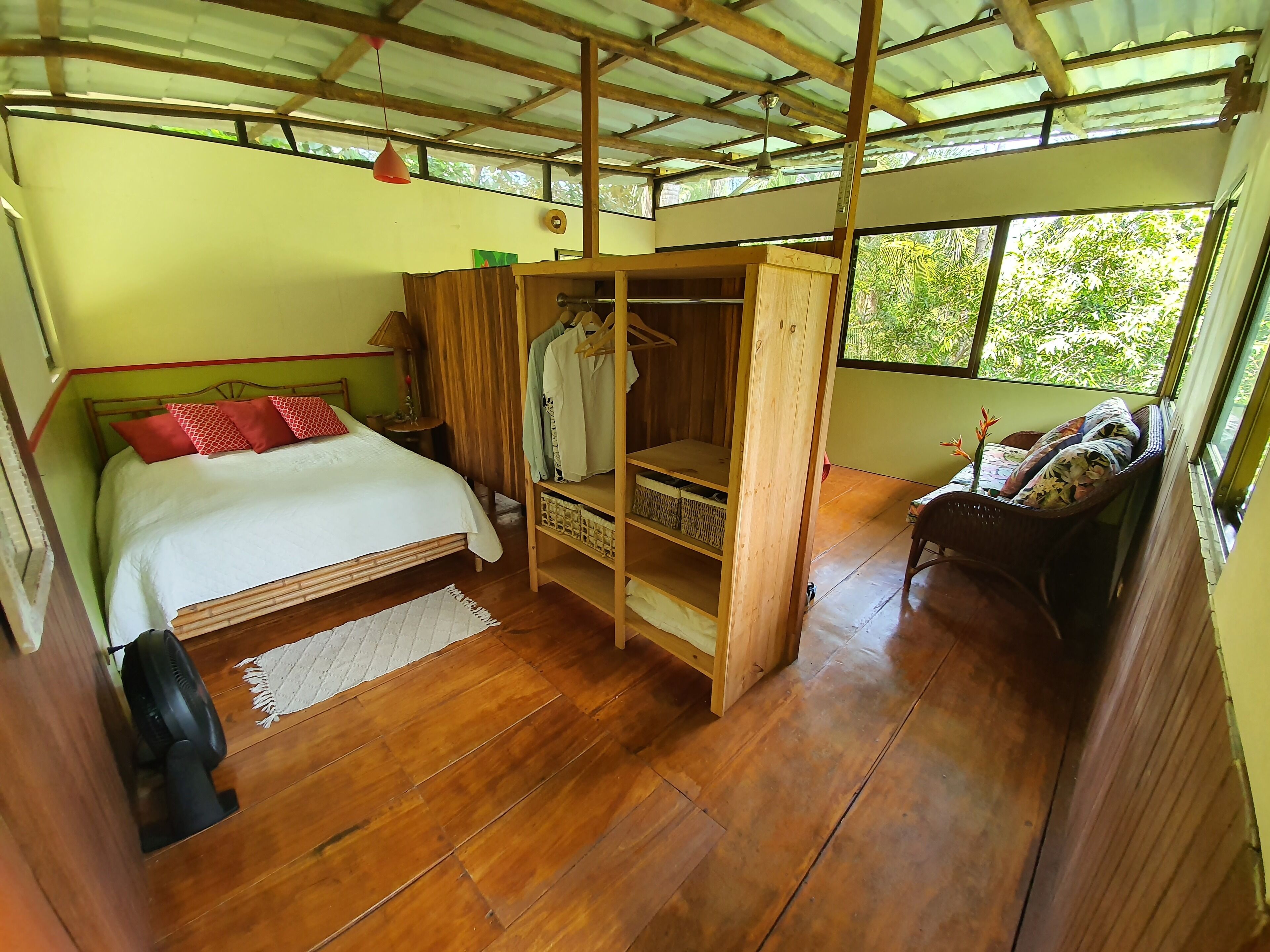 A room with a bed, wooden furniture, a wardrobe, and a window with a view of greenery.