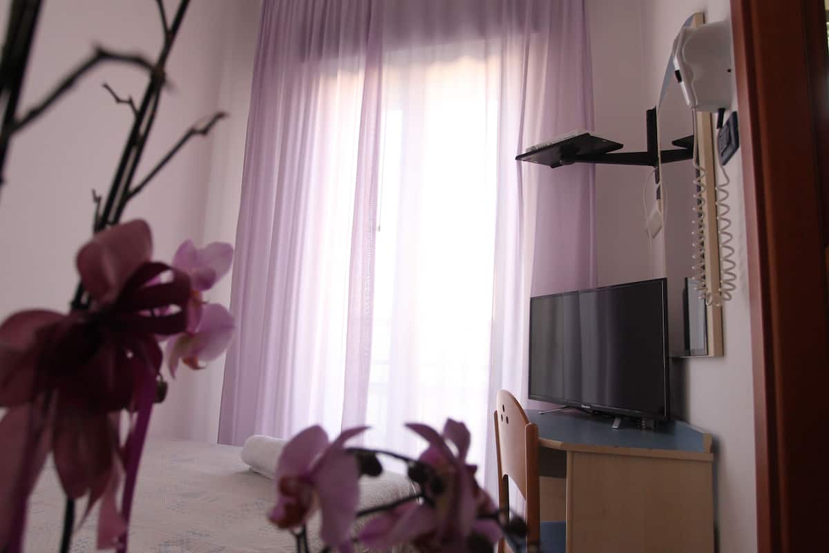 A room with a bed, a TV on a stand, a telephone, and a window with curtains.