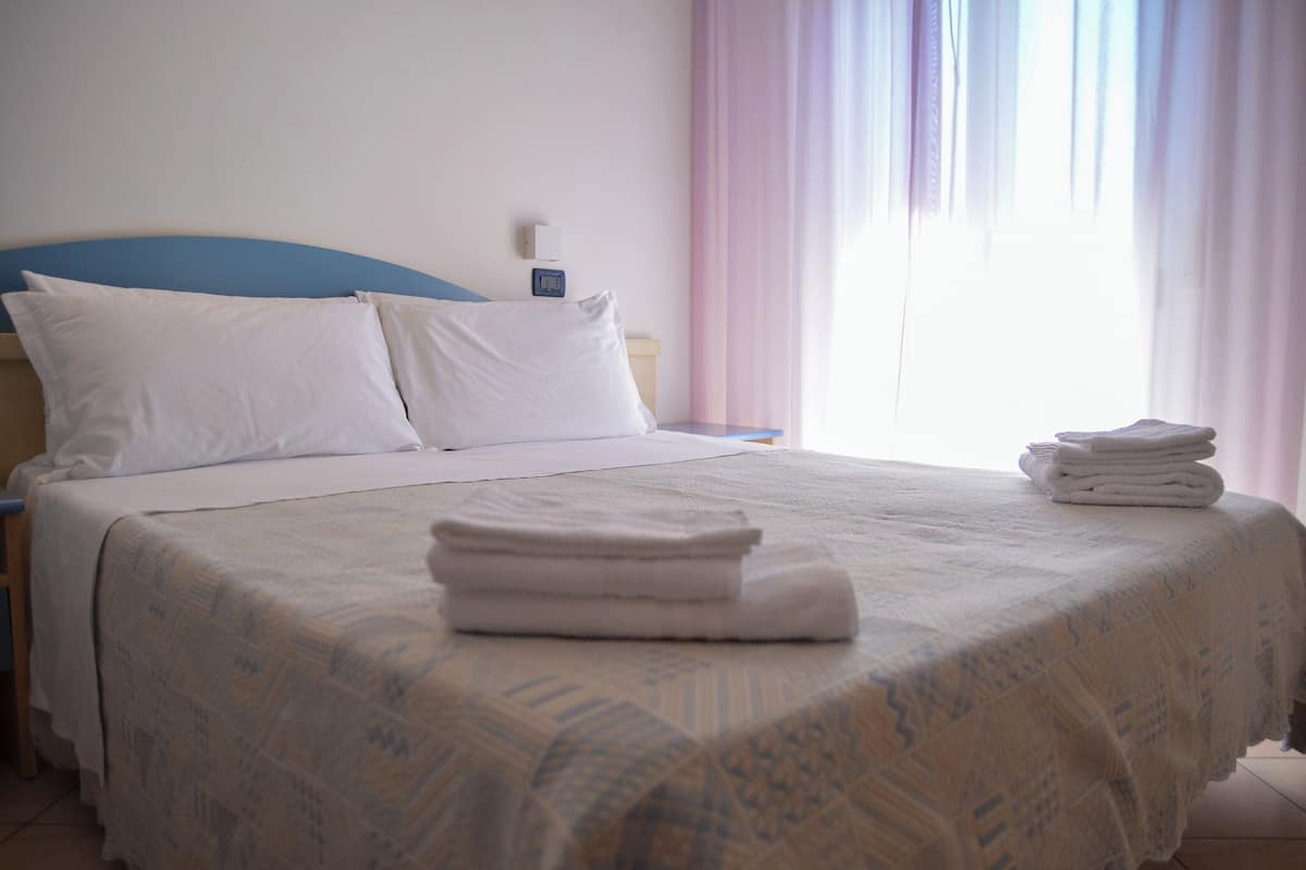 A neatly made bed with a patterned bedspread, two pillows, and folded towels on the bed.