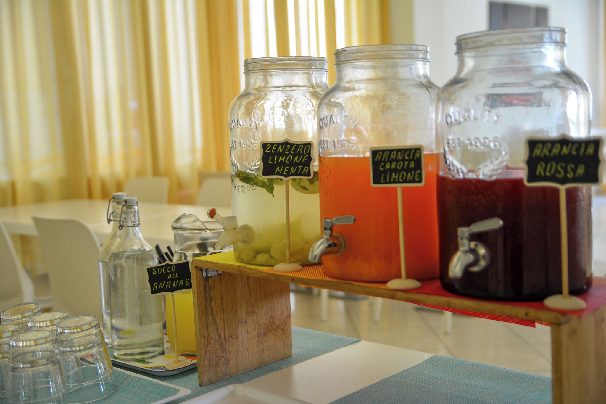 Un présentoir à boissons avec trois bocaux étiquetés : « Zenzero Limone Menta », « Arancia Carota Limone » et « Arancia Rossa ».