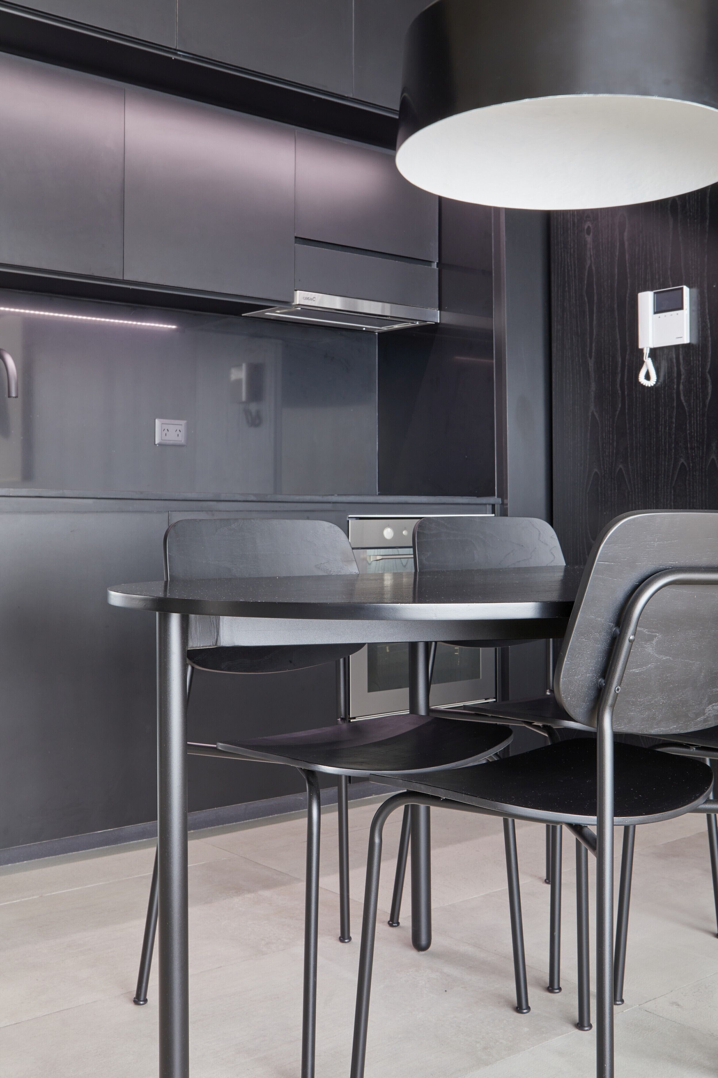 Een moderne keuken met donkere kastjes, een roestvrijstalen afzuigkap en een ronde eettafel met vier stoelen.