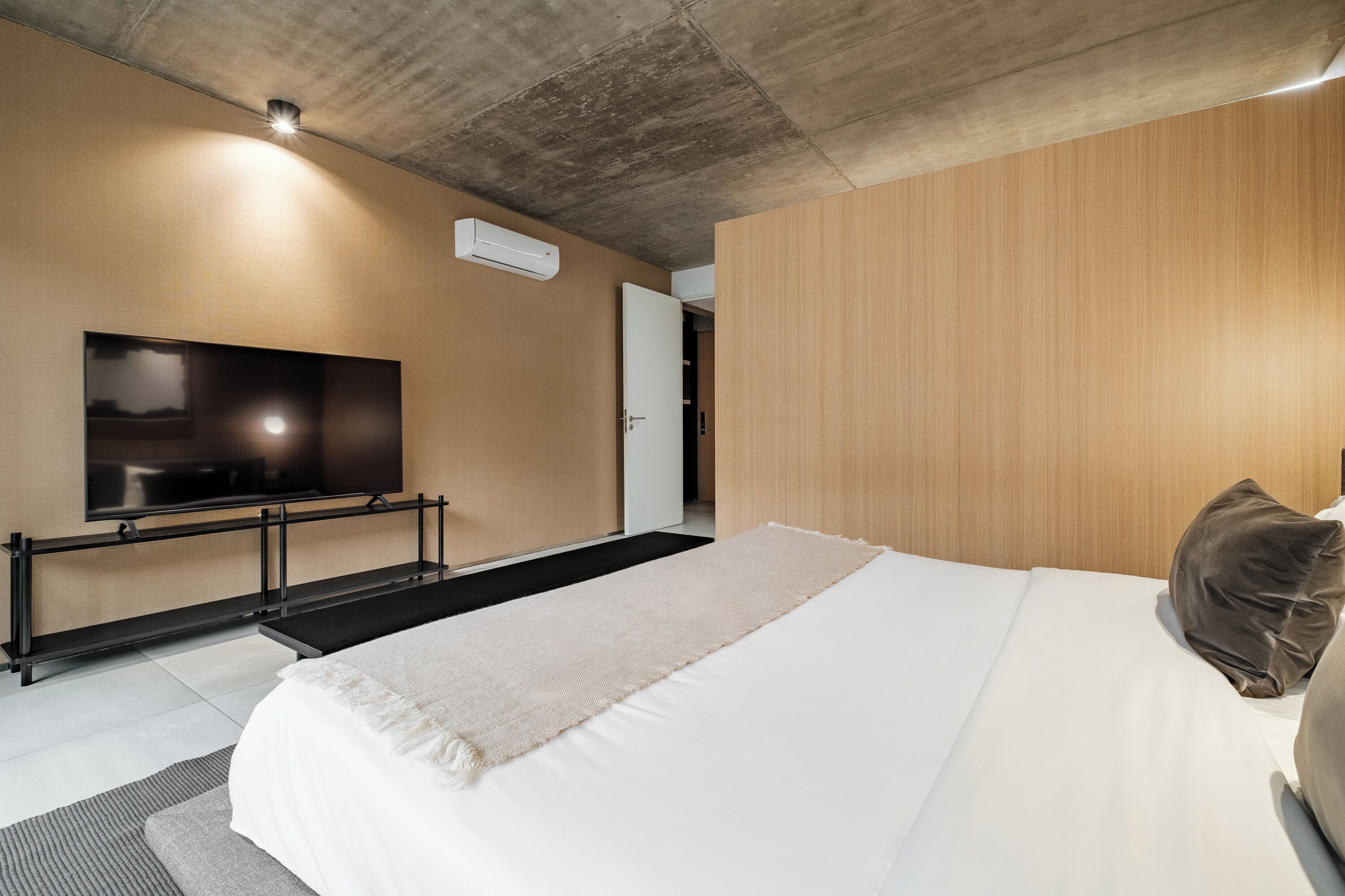 A modern hotel room with a large bed, a flat-screen TV mounted on the wall, and a wooden panel wall.