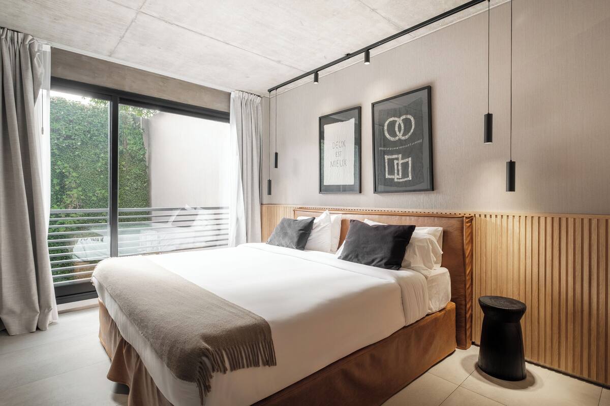A modern bedroom with a large bed, a wooden headboard, a small stool, and two framed pictures on the wall.