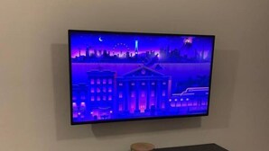 Un téléviseur fixé au mur, au-dessus d’un meuble de rangement noir agrémenté de panneaux décoratifs.