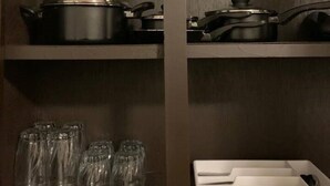 Une cuisine avec des meubles de rangement en bois foncé, deux casseroles noires sur l’étagère supérieure et un plateau blanc contenant des ustensiles sur l’étagère inférieure.