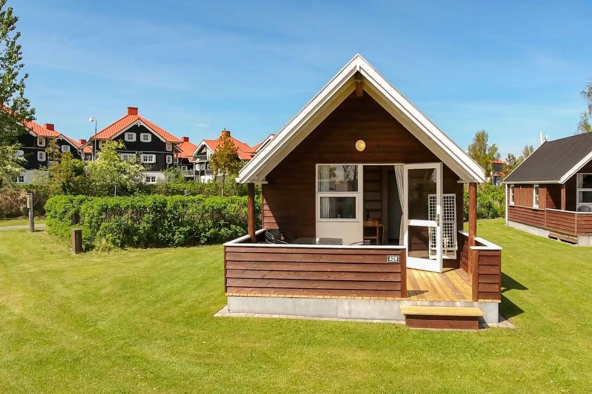 A small wooden cabin with a sloped roof, a porch, and a large window.