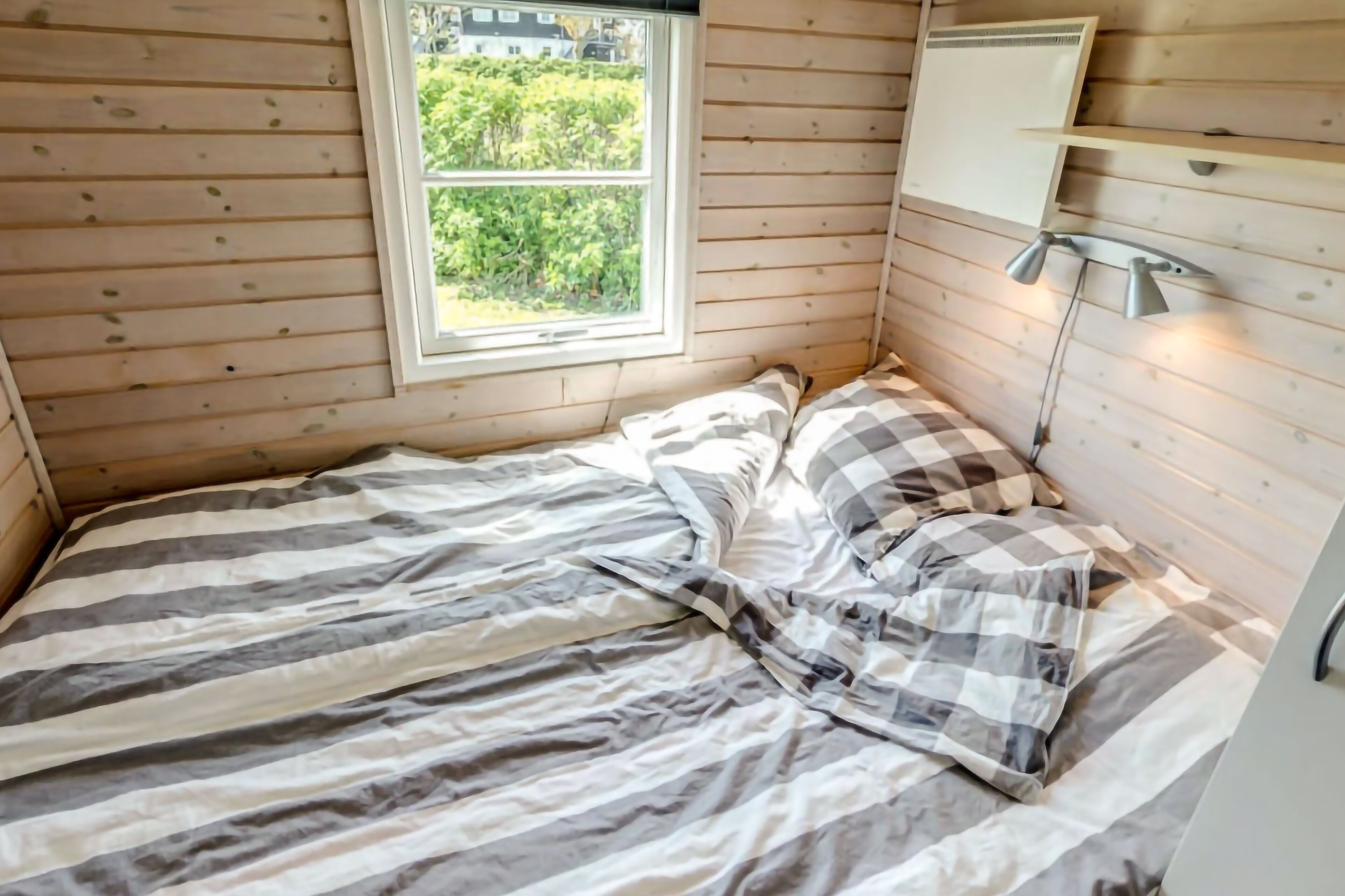A small bedroom with a single bed, a window, and a bedside lamp.
