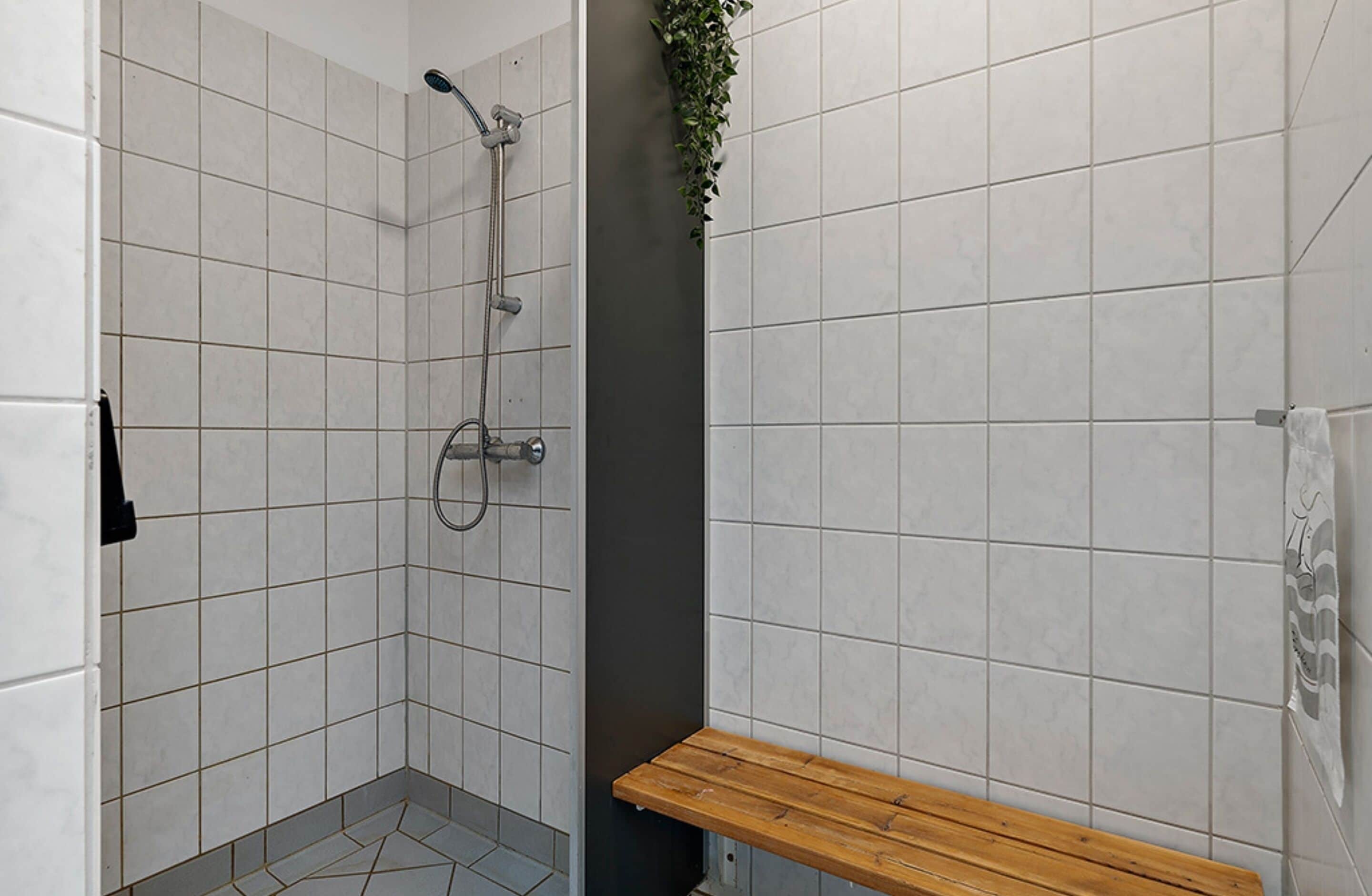 A small, tiled shower area with a wooden bench and a showerhead.