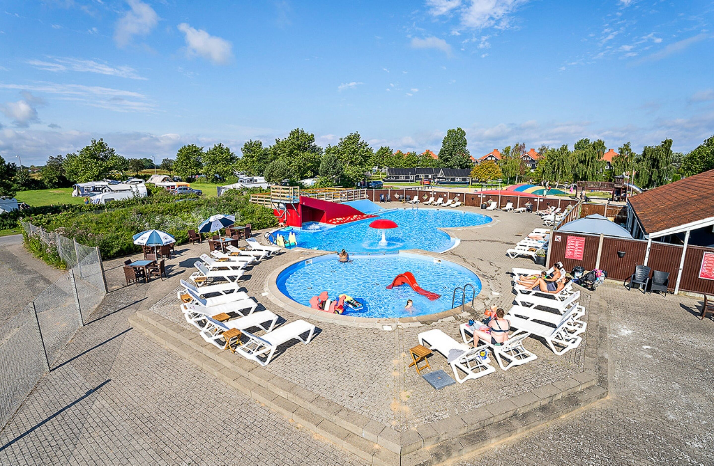 A swimming pool area with multiple pools, lounge chairs, and umbrellas.