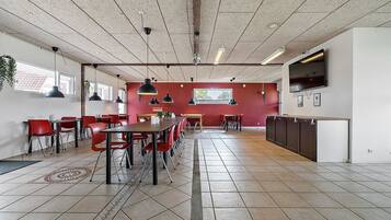 A spacious dining area with red chairs and tables, a kitchen area with cabinets, and a television mounted on the wall.