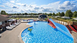 Una gran piscina con tobogán, sillas de descanso y un edificio al fondo.