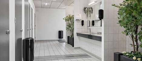 A modern bathroom with a tiled floor, a sink area with a mirror, and two potted plants.