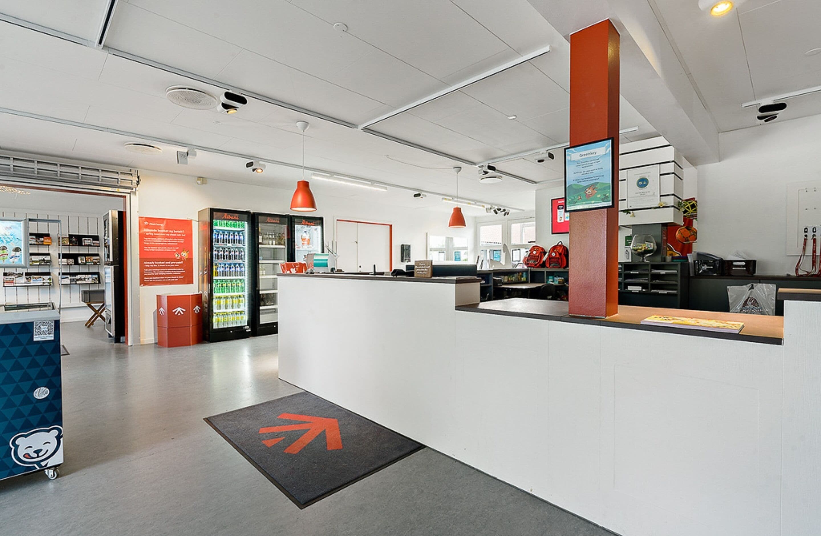 A modern reception area with a counter, a beverage fridge, and directional arrows on the floor.