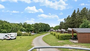 A campsite with RVs parked on a dirt road, surrounded by greenery and a wooden building with outdoor seating.
