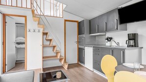 A modern kitchen with grey cabinets, a built-in oven, and a coffee maker. There is a wooden staircase leading to a lofted area.