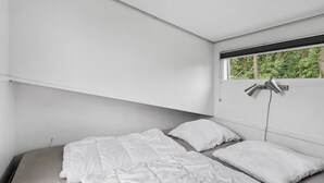 A minimalist bedroom with a single bed, white bedding, and a window with a view of trees.