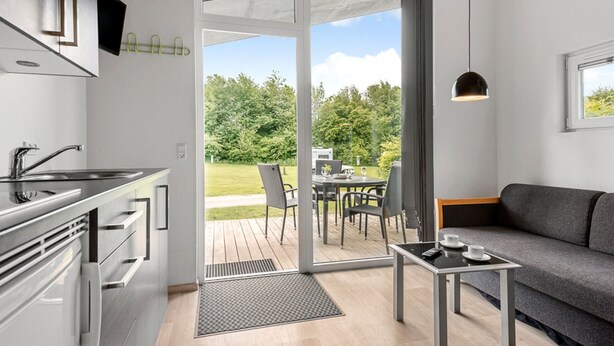 A modern kitchen with a built-in oven, a dining area with a table and chairs, and a sofa.
