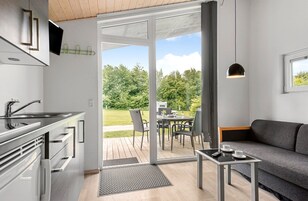 Et moderne køkken med indbygget ovn, et spiseområde med bord og stole, samt en sofa.