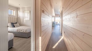 A narrow hallway with wooden paneling, a bed with a gray headboard, and a window with blinds.