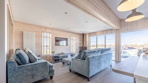A spacious living room with two sofas, a flat-screen TV, and a large window offering a view.