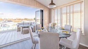 A dining area with a glass table, white chairs, and a view of boats through large windows.