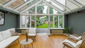 A conservatory with a sloped roof, wooden flooring, wicker furniture, and a view of a garden. - 4 Bed Family Home In Windsor - By Tempstay (Old Windsor)
