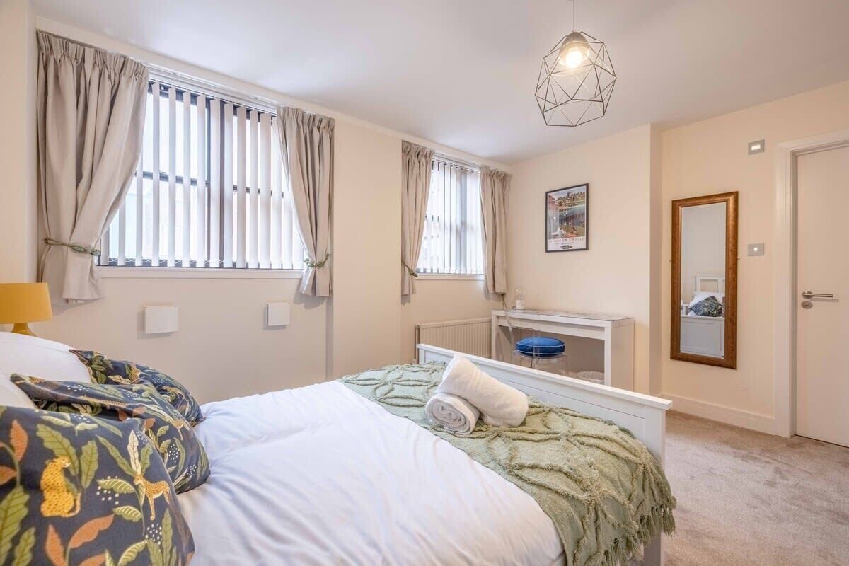 A bedroom with a bed, a bedside table, a mirror, and a window with curtains.