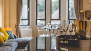 A room with a dining table, a sofa, and a champagne bucket with glasses. - Windsor Castle Views & Parking - By Tempstay (Berkshire)