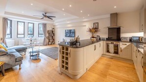 A modern kitchen with a central island, built-in appliances, and a dining area with a sofa and table. - Windsor Castle Views & Parking - By Tempstay (Berkshire)