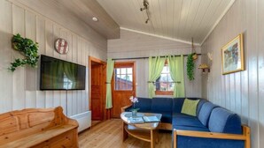 A cozy room with wooden walls, a blue sofa, a wooden bench, a flat-screen TV, and a small table with a plant. - First Camp Bø  Telemark (Midt-Telemark)