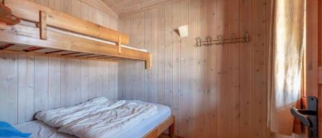 A wooden cabin room with a bunk bed, wooden walls, and a door with a towel hanging.