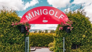 A red archway with "MINIGOLF" and a golf flag, surrounded by greenery and bushes. - First Camp Bø  Telemark (Midt-Telemark)