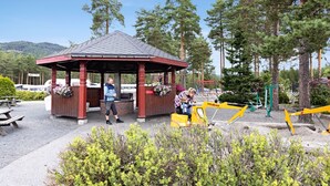 A gazebo with a red roof and wooden pillars, surrounded by greenery and trees. - First Camp Bø  Telemark (Midt-Telemark)