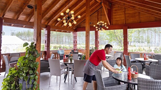 An outdoor patio with wooden beams, wicker furniture, and hanging light fixtures. - First Camp Bø  Telemark (Midt-Telemark)