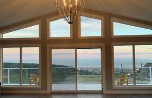 A spacious room with large windows offering a view of a landscape and a body of water. - Alma Ocean Breeze - Brand New Cottage (Alma)