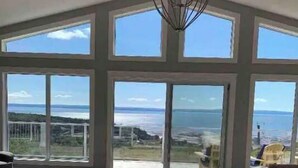 A room with large windows offering a view of the sea and hills.